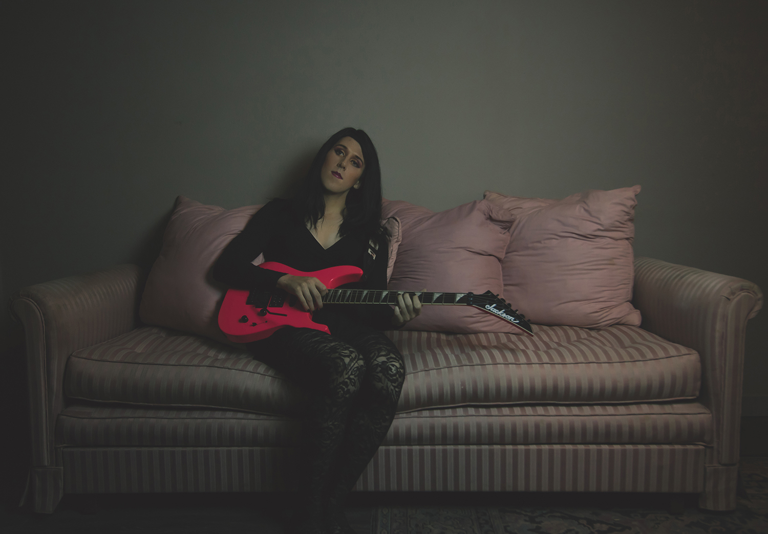 Photo of Shelly Webster sitting on a couch with an electric guitar.